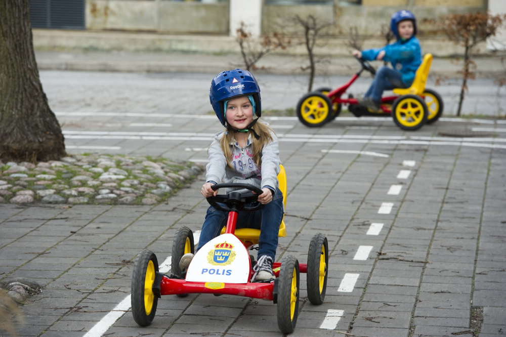 Två barn kör trampbilar på Polismuseets trafiklekplats som finns på gården utanför polismuseet.