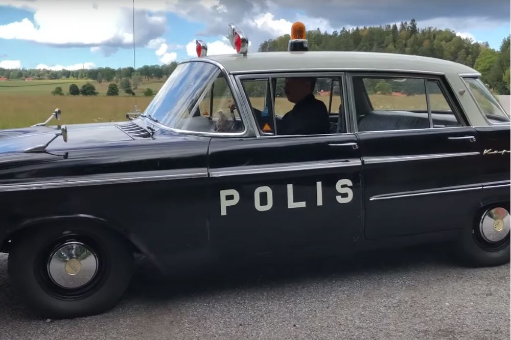 En Opel Kapitän som polisbil, öppna landskap i bakgrund.